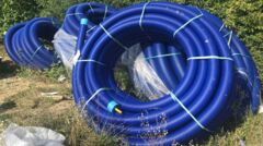 Zvinuté predizolované rúry WATTS Microflex s vlnitým modrým vonkajším plášťom, zabezpečené popruhmi a uložené vonku pred inštaláciou.