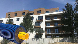 WATTS Microflex pre-insulated pipe with a corrugated blue outer casing and yellow inner pipe, overlaid on an image of a modern multi-story residential building under construction.