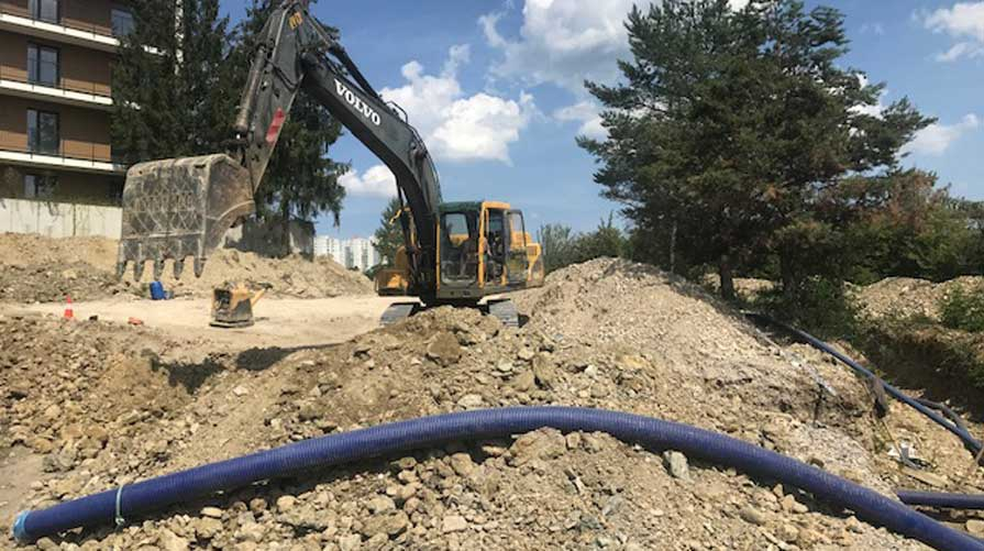 Wykopy koparką Volvo i rury preizolowane WATTS Microflex ułożone w otwartym wykopie, przygotowane do instalacji podziemnej.
