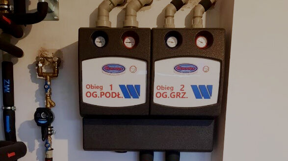 WATTS HK25 and HKM25 pump groups installed on a heating system in a Polish house, featuring insulated casings, pressure gauges, and labeled circuits for underfloor and radiator heating.