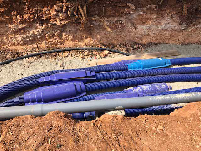 Construction site with partially built single-story brick structures and excavated red soil, prepared for the installation of WATTS Microflex pre-insulated piping.