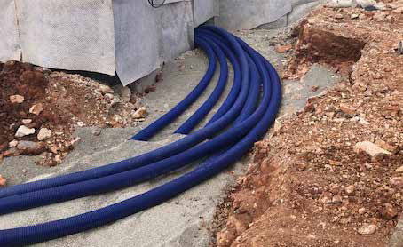Construction site with partially built single-story brick structures and excavated red soil, prepared for the installation of WATTS Microflex pre-insulated piping.