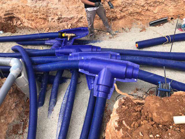 Construction site with partially built single-story brick structures and excavated red soil, prepared for the installation of WATTS Microflex pre-insulated piping.