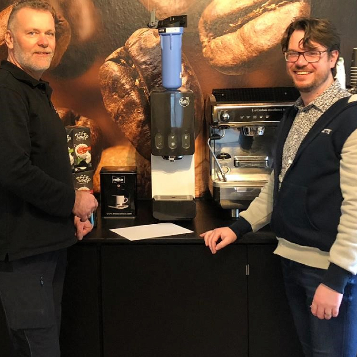Twee mannen naast koffiemachine