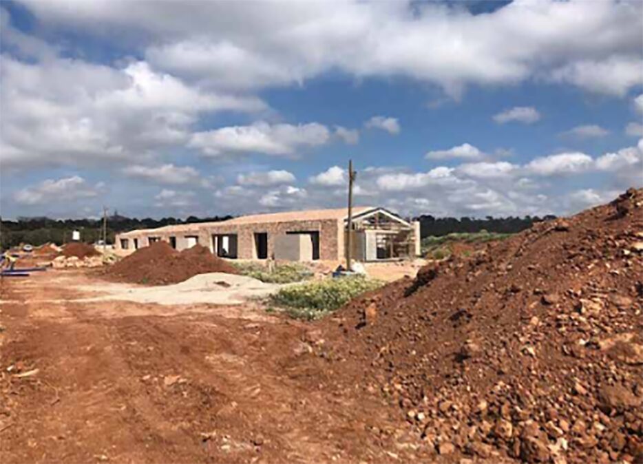 Construction site with partially built single-story brick structures and excavated red soil, prepared for the installation of WATTS Microflex pre-insulated piping.