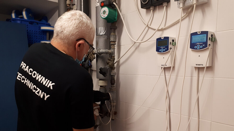 Pracownik techniczny wykonujący konserwację instalacji hydraulicznej wyposażonej w elektroniczne zawory mieszające WATTS e-ULTRAMIX. Dwa sterowniki są zamontowane na ścianie