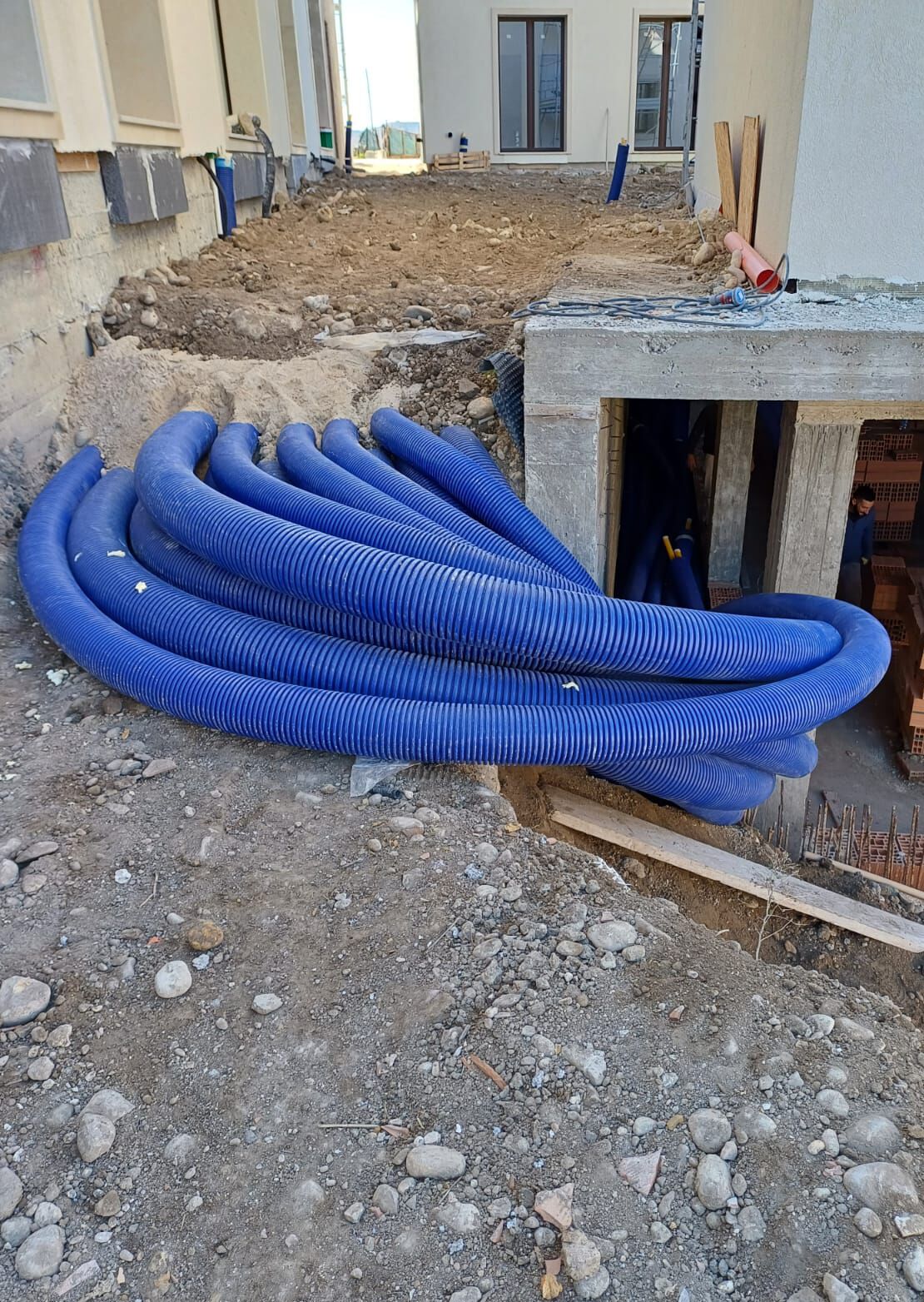 Tubi preisolati WATTS Microflex® avvolti in un cantiere, pronti per l'installazione sotterranea in una rete di riscaldamento e raffrescamento residenziale.