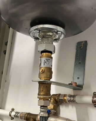 Close-up view of a boiler system with an anti-Legionella valve, brass fittings, and connected pipes mounted on a white wall.