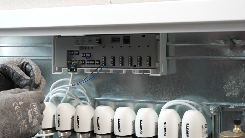Ein Installateur verkabelt den Watts Vision Regelverteiler WFC-03 mit Stellantrieben 26LC, die auf dem Heizkreisverteiler HKV2013AF installiert sind.