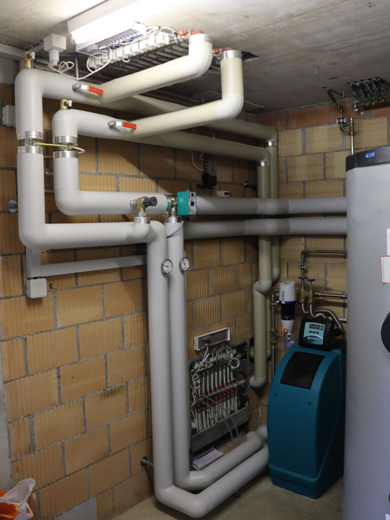 Technikraum mit installierter Sole-Wasser-Wärmepumpe, Watts Vision Wireless Regelung, isolierten Rohrleitungen und Heizkreisverteiler in einem 2-Familienhaus am Murtensee Schweiz.