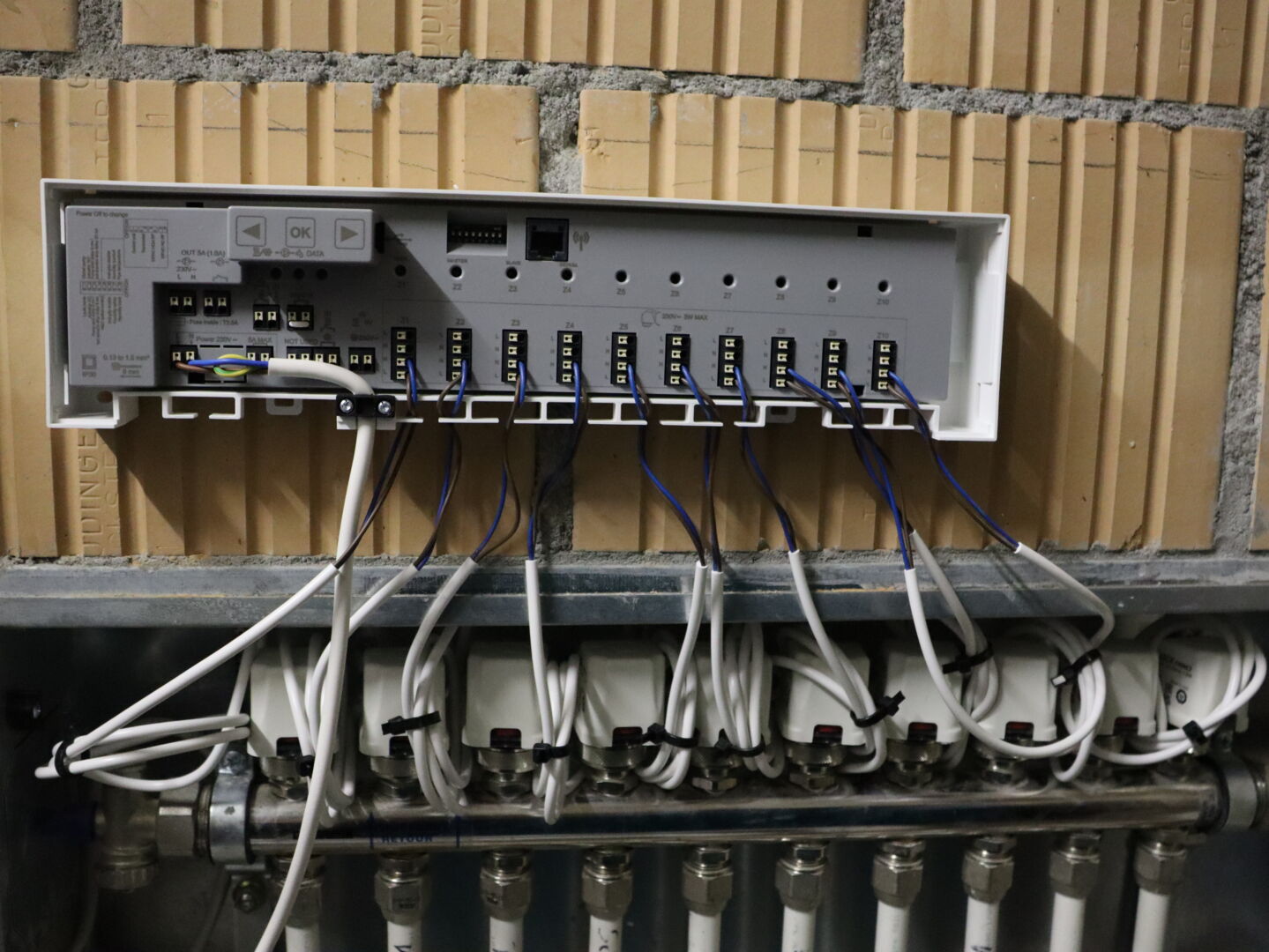 WATTS Regelverteiler WFC-03 10Z HC RF mit verkabelten Stellantrieben 22CX auf einem Heizkreisverteiler, montiert an einer Ziegelwand.
