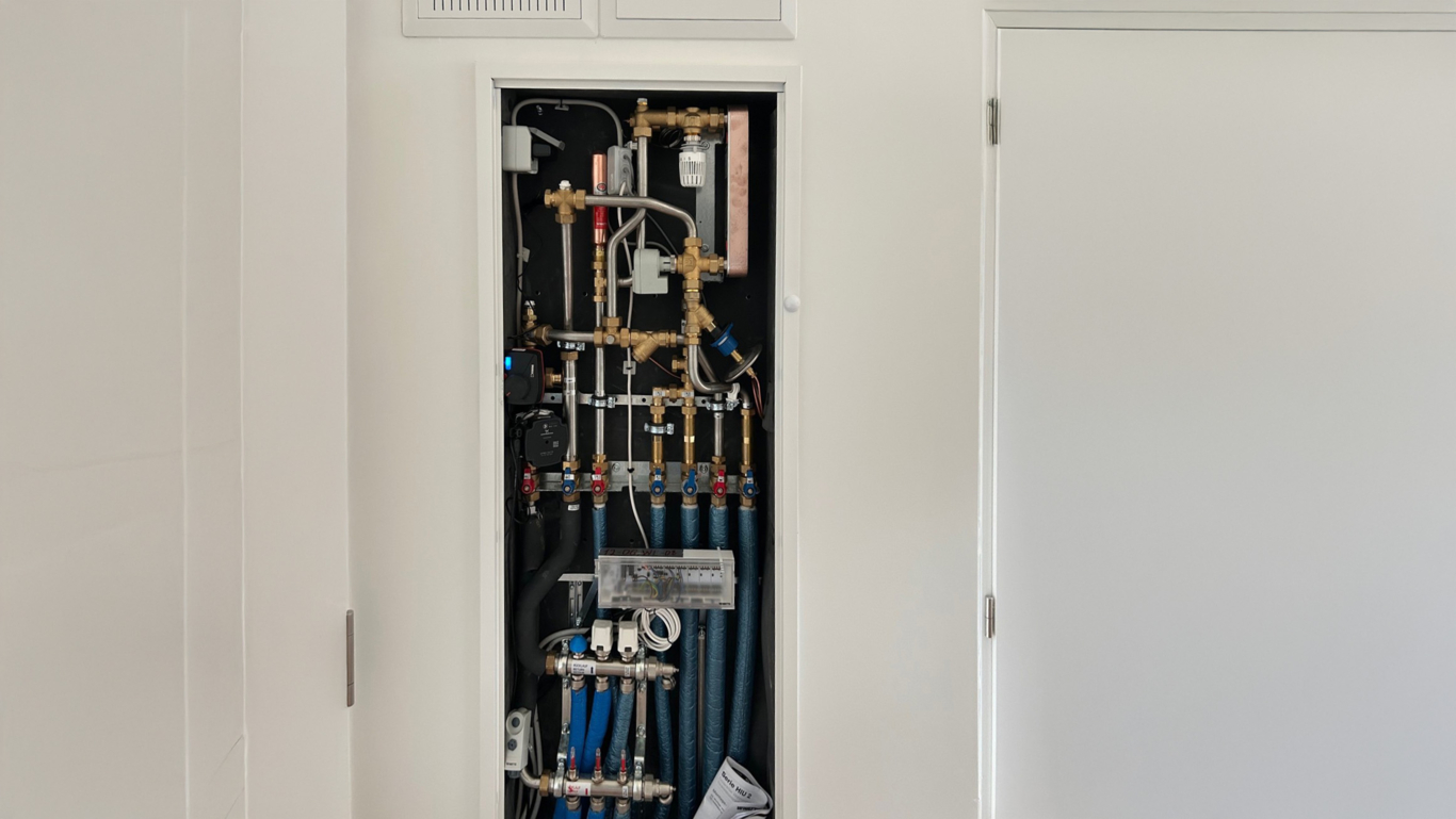 Installed HIU2 HKM heat interface unit with stainless steel heating manifold inside flush-mounted system cabinet.