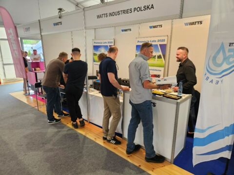 Prezentacja produktów Watts podczas targów branżowych, odwiedzający rozmawiają z przedstawicielami firmy.